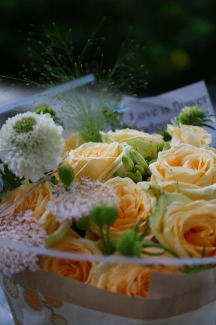 A bouquet arrangement of fresh, pale peach roses and white blooms, including vibrant green buds and small, round, fluffy white flowers, possibly chrysanthemums or carnations. The flowers are arranged 